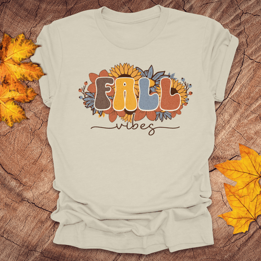 Beige t-shirt with 'Fall vibes' design on a wooden surface with fall leaves.