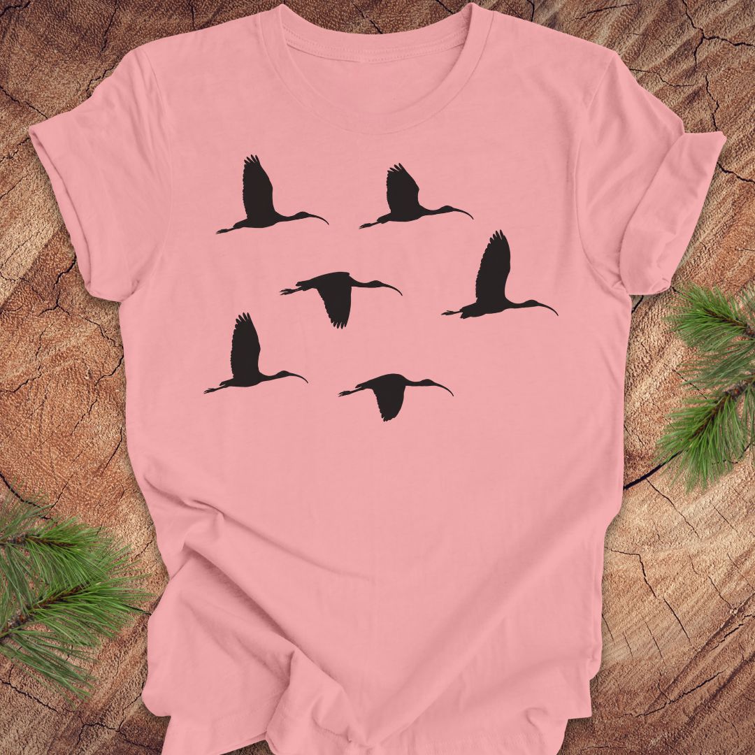 Pink t-shirt with black ibis bird silhouettes on a wooden surface