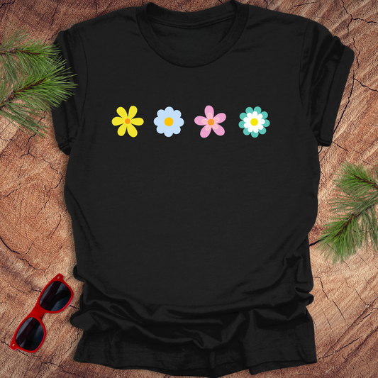 Black t-shirt with colorful flower designs on a wooden surface with sunglasses and greenery.