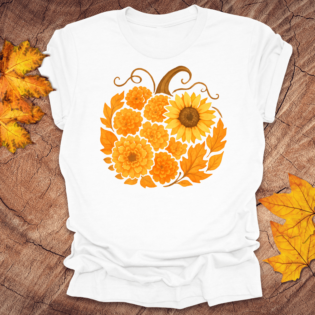 White t-shirt with a floral pumpkin design on a wooden surface with fall leaves.