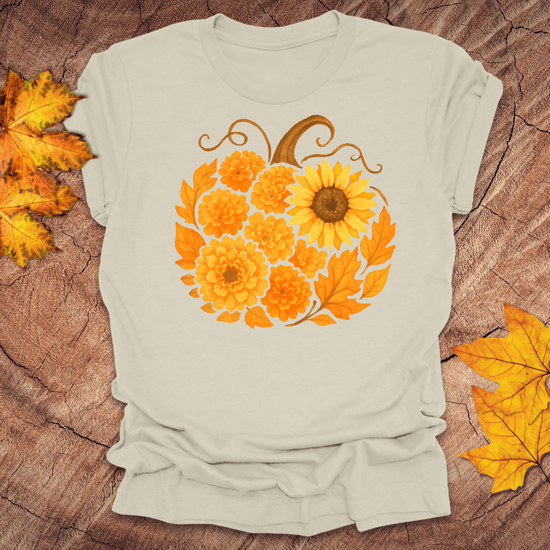 Beige t-shirt with a pumpkin design made of sunflowers on a wooden surface with autumn leaves.