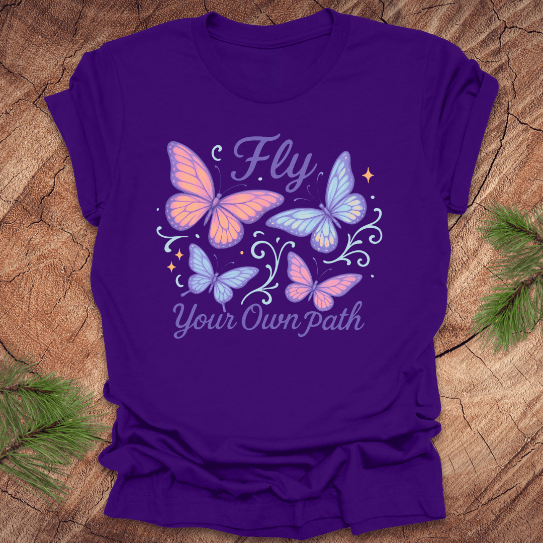 Purple t-shirt with butterfly design and 'Fly Your Own Path' text on a wooden surface.