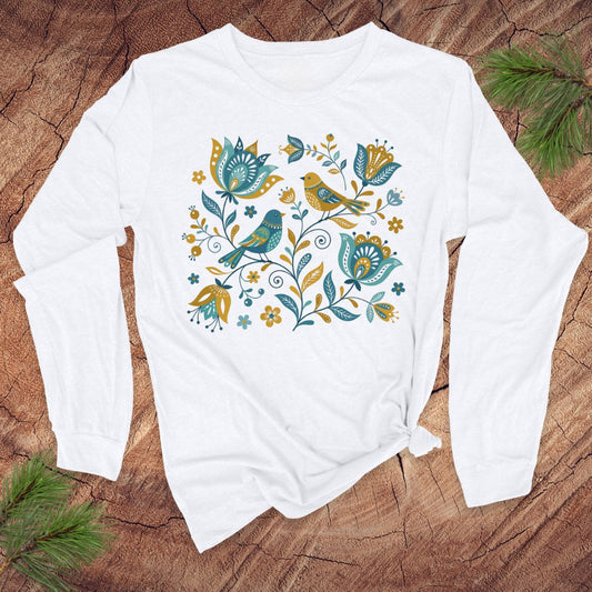 White long-sleeve tshirt with folk art floral and bird design on a wooden surface