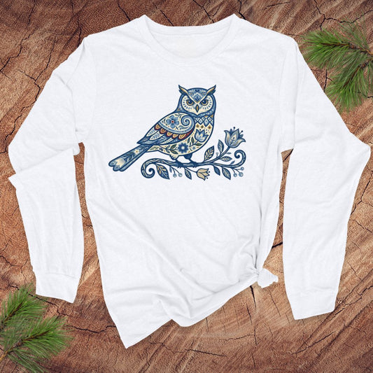 White long-sleeve shirt with a blue folk art floral owl design on a wooden surface.