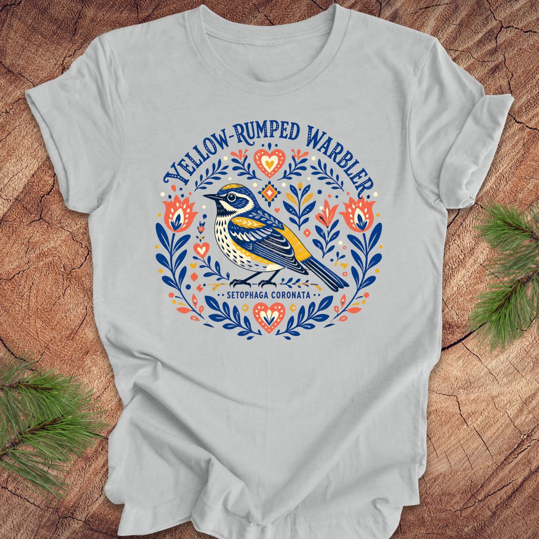 Gray t-shirt with a folk art yellow rumped warbler design on a wood background.