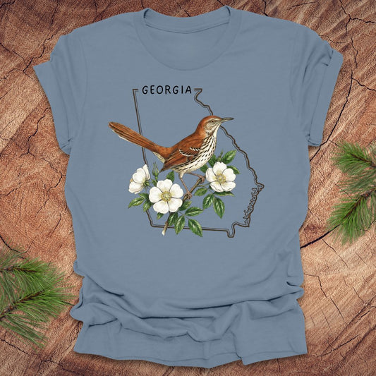 Steel blue t-shirt with the outline of the state of Georgia and state bird and flower, brown thrasher and cherokee rose on a wooden surface