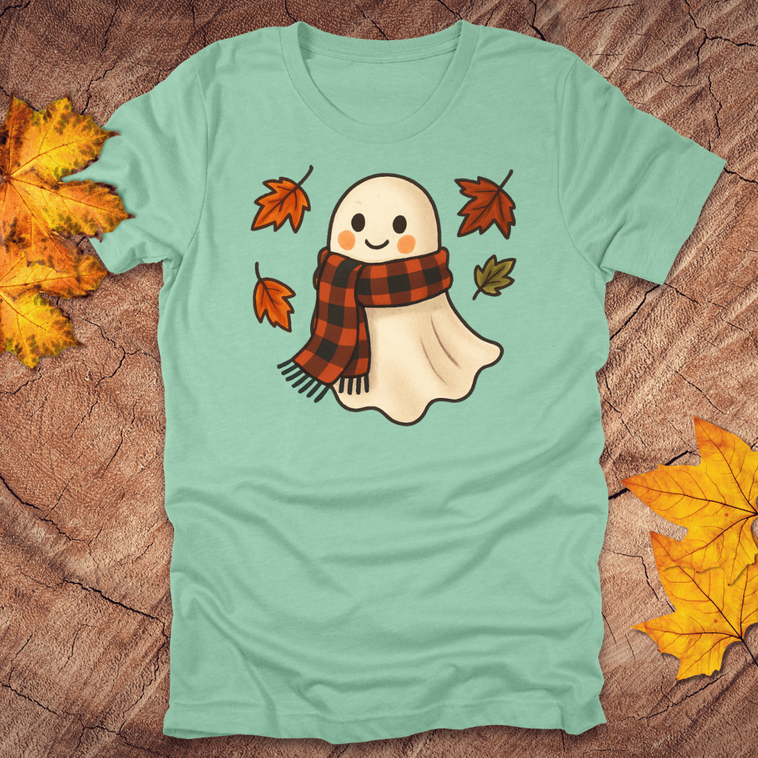 mint green t-shirt with a ghost wearing a plaid scarf design on a wooden surface with autumn leaves.