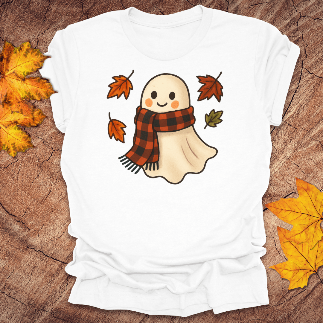 White t-shirt with a ghost wearing a plaid scarf design on a wooden surface with autumn leaves.