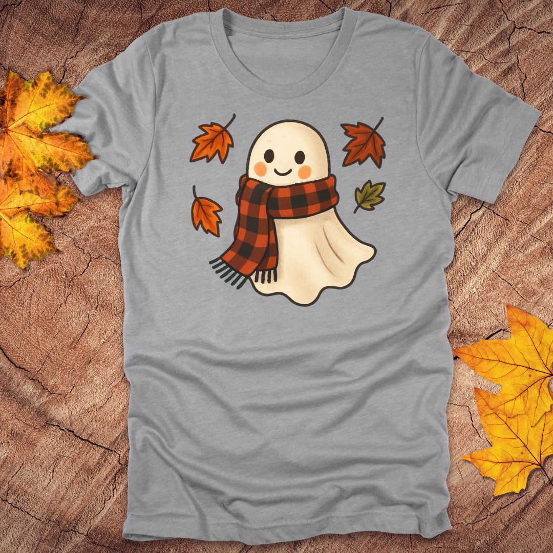 Gray t-shirt with a ghost wearing a plaid scarf design on a wooden surface with autumn leaves.