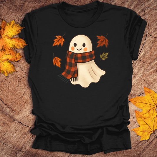 Black t-shirt with a ghost wearing a plaid scarf design on a wooden surface with autumn leaves.