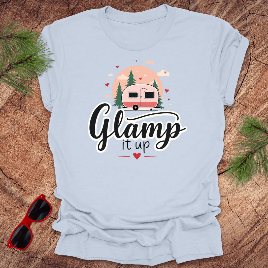 Light blue t-shirt with 'Glam it up' text and camper graphic on a wooden surface with sunglasses and greenery.