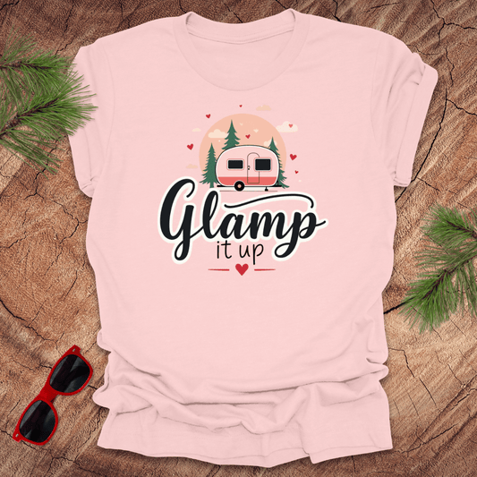 Pink t-shirt with 'Glam it up' text and camper graphic on a wooden surface with sunglasses and greenery.