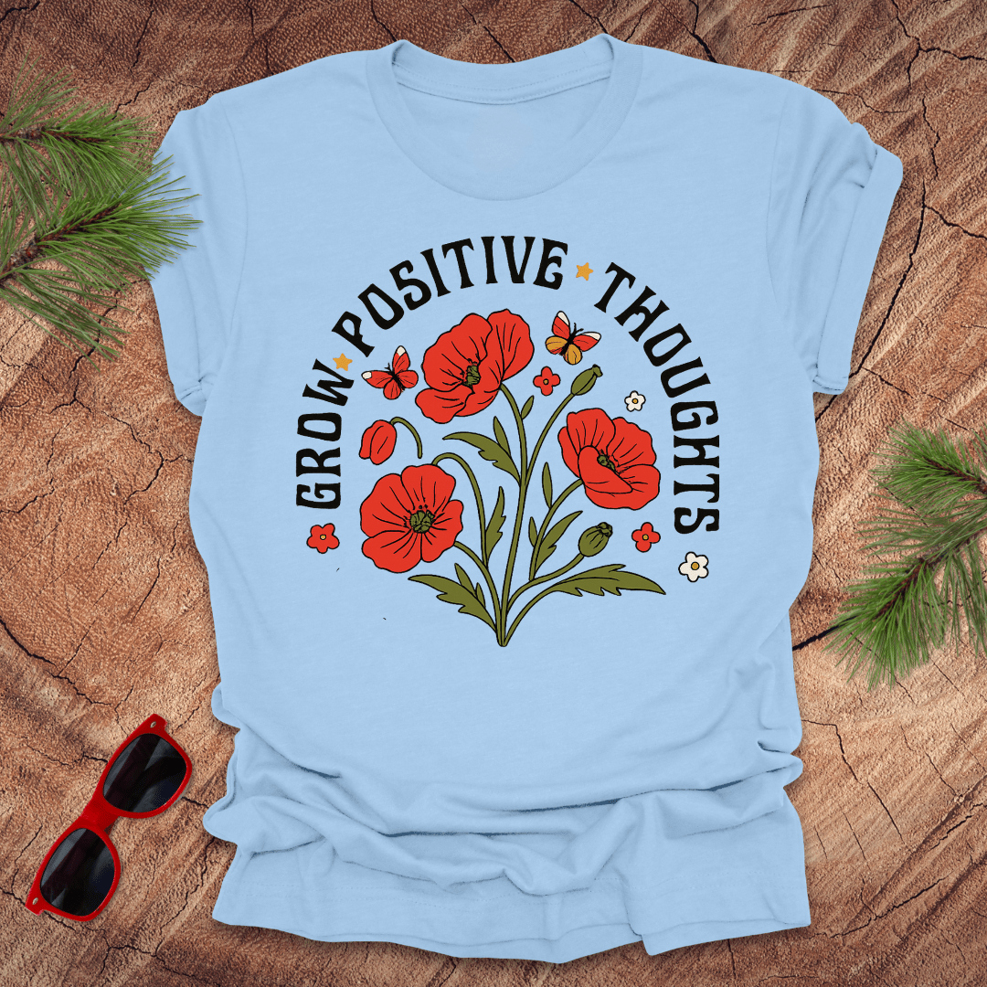 baby blue t-shirt with red flowers and text on a wooden surface with sunglasses and greenery.