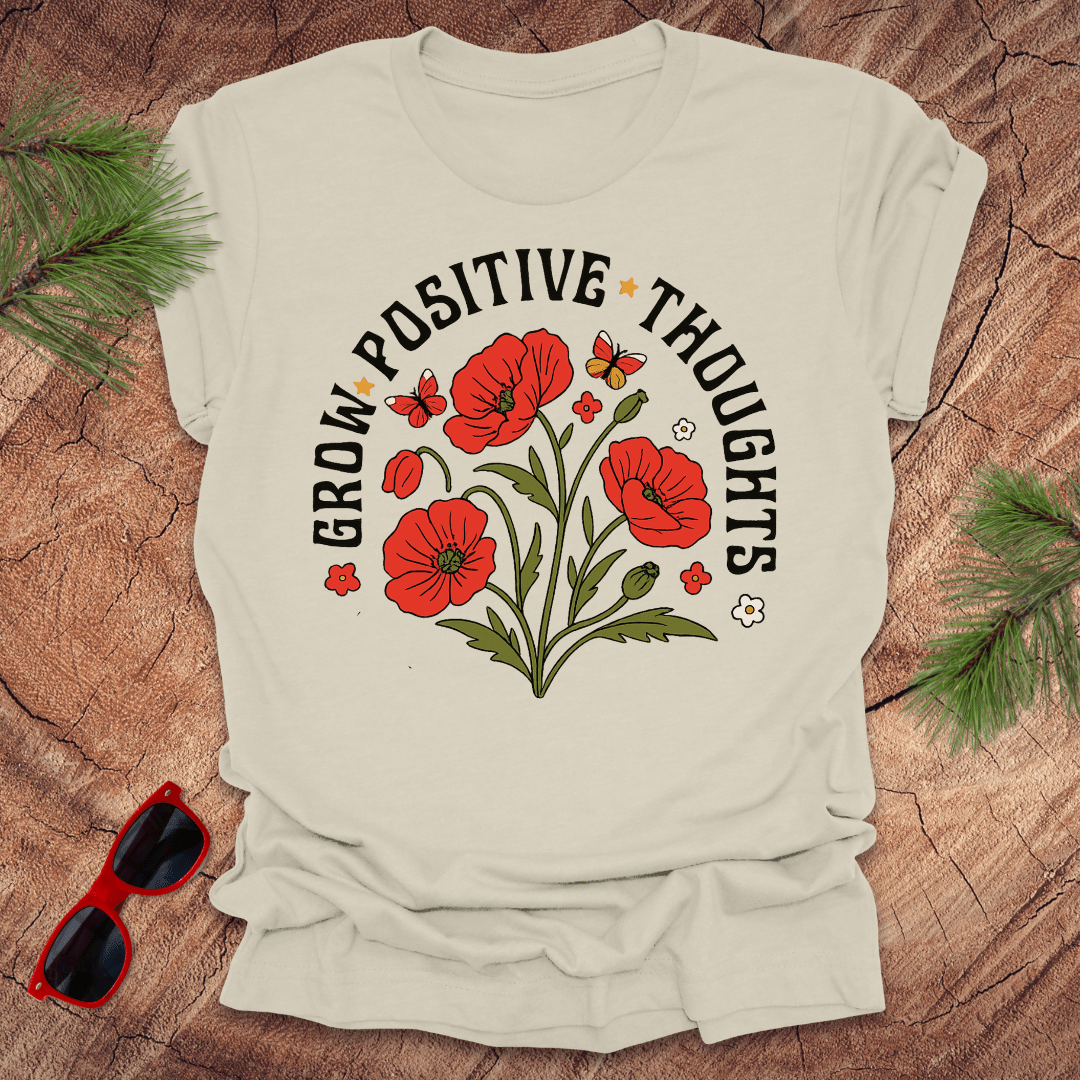 Beige t-shirt with red flowers and text on a wooden surface with sunglasses and greenery.