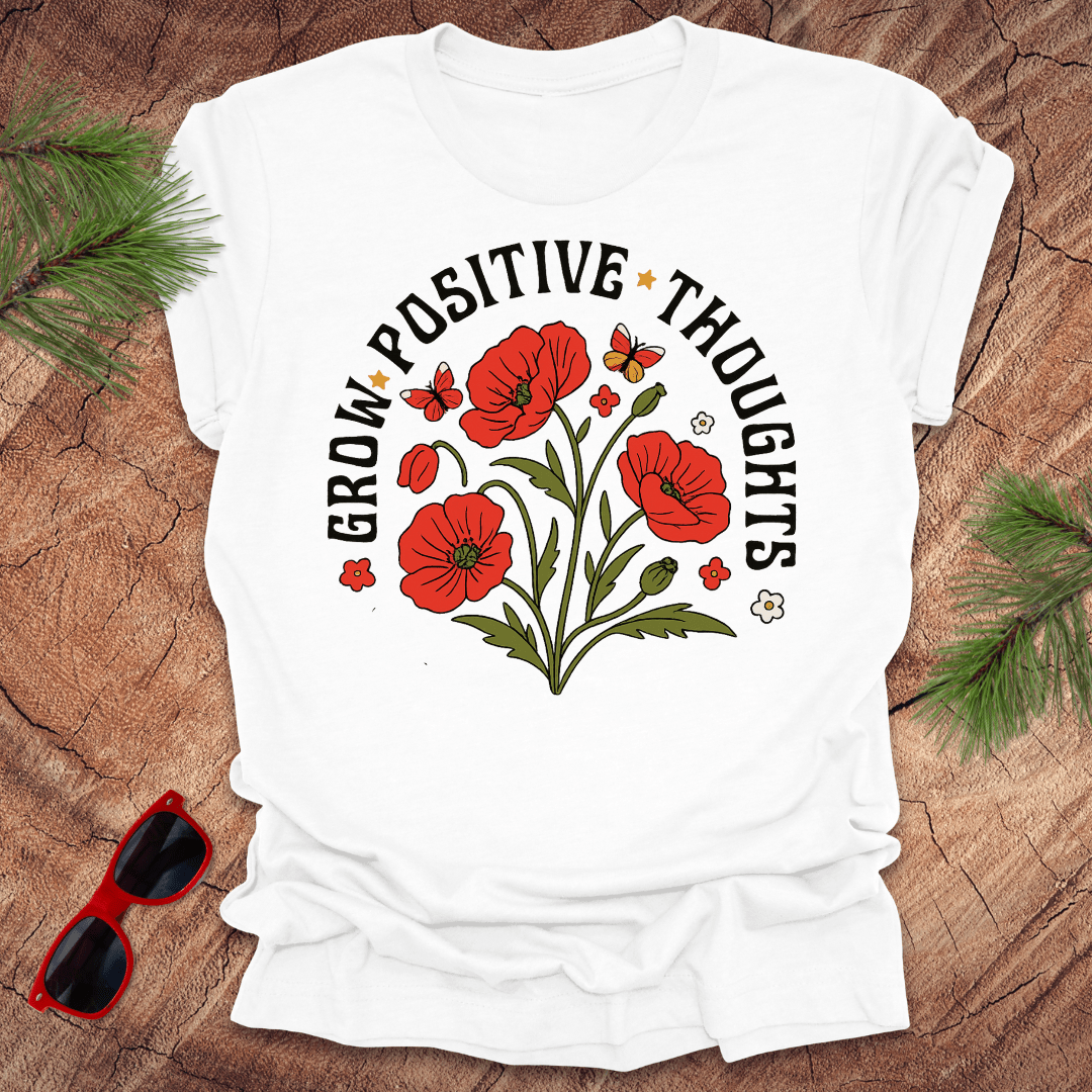 White t-shirt with red floral design and text on a wooden surface with sunglasses and greenery.