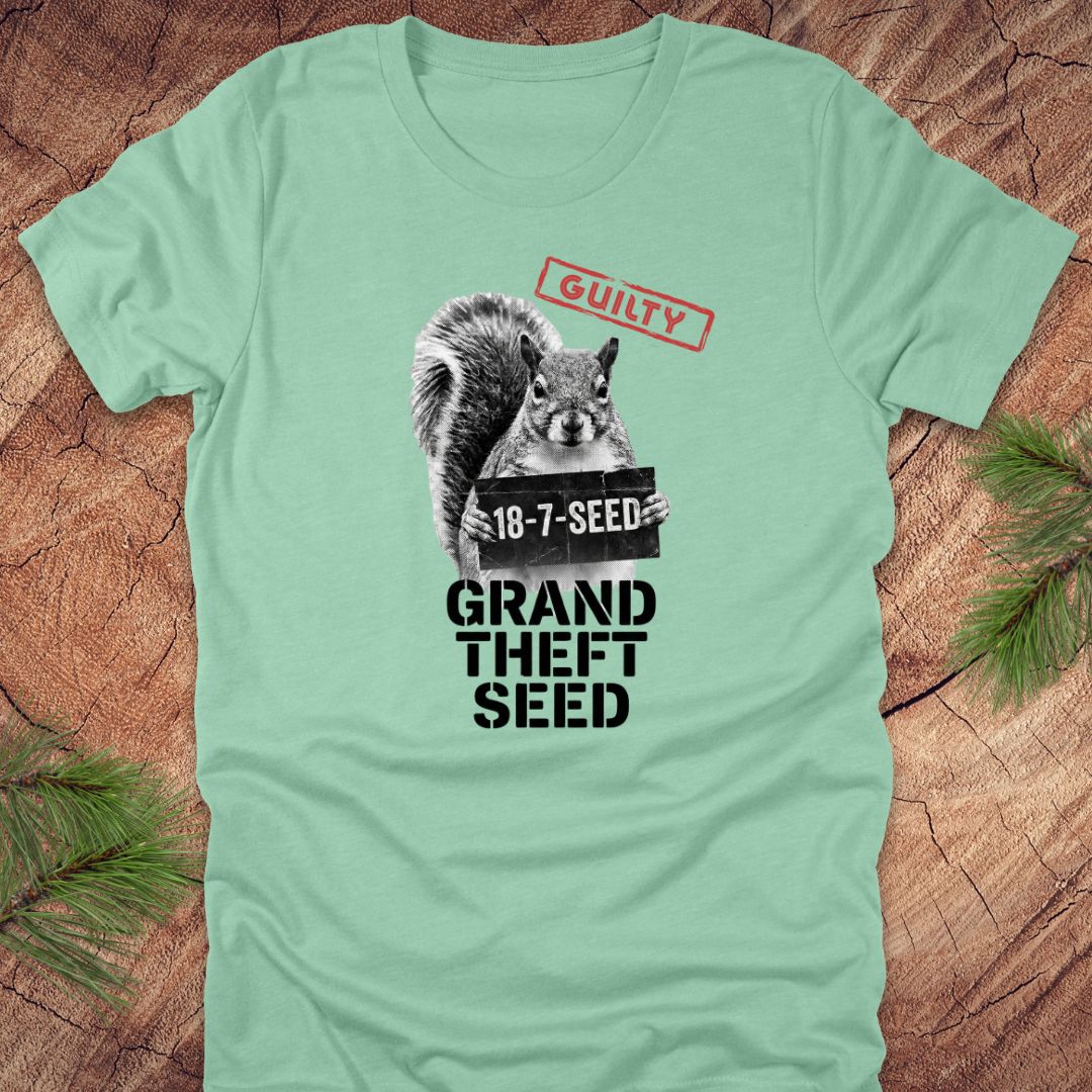 Mint green t-shirt with a squirrel holding a seed packet graphic and text, 'guilty. grand theft seed'on a wooden surface.