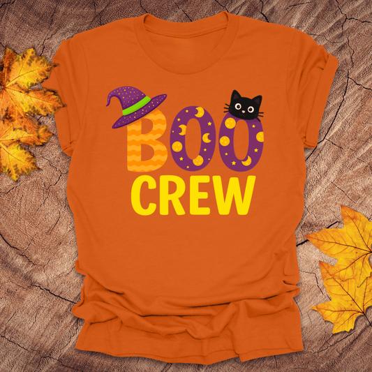 Orange t-shirt with 'BOO CREW' text and Halloween graphics on a wooden surface with leaves.