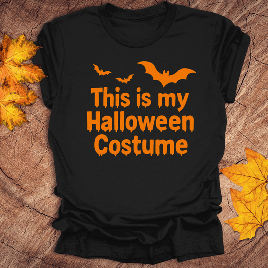 Black t-shirt with 'This is my Halloween Costume' text and bats on a wooden surface with leaves.