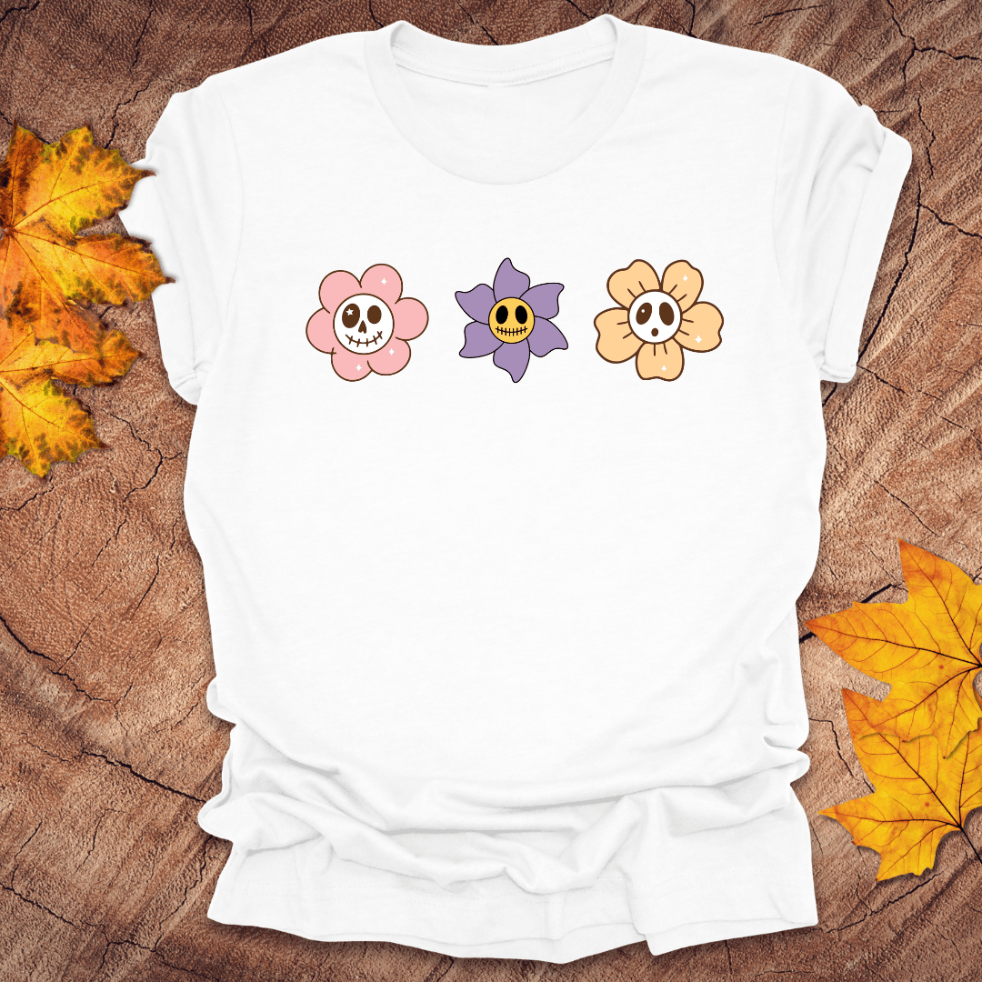 White t-shirt with colorful skull flower designs on a wooden surface with autumn leaves.