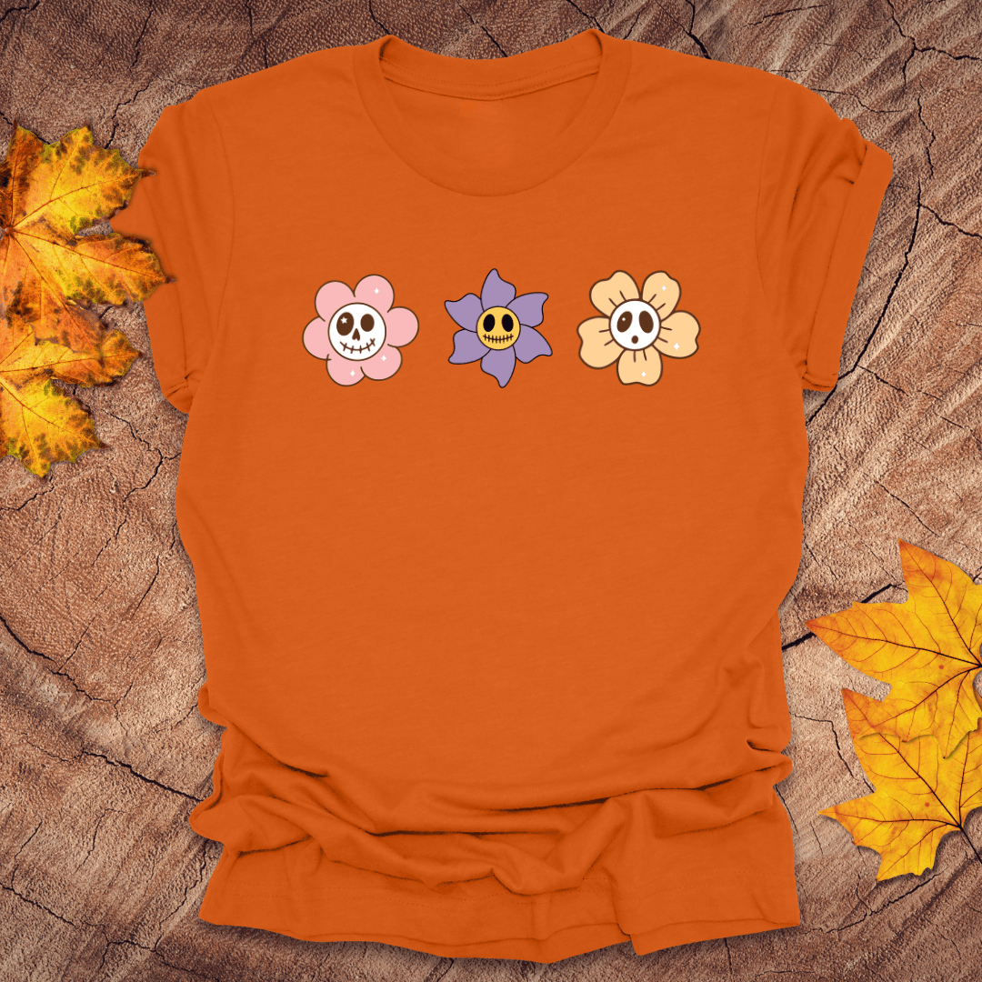 Orange t-shirt with cartoon skull flowers on a wooden surface with autumn leaves