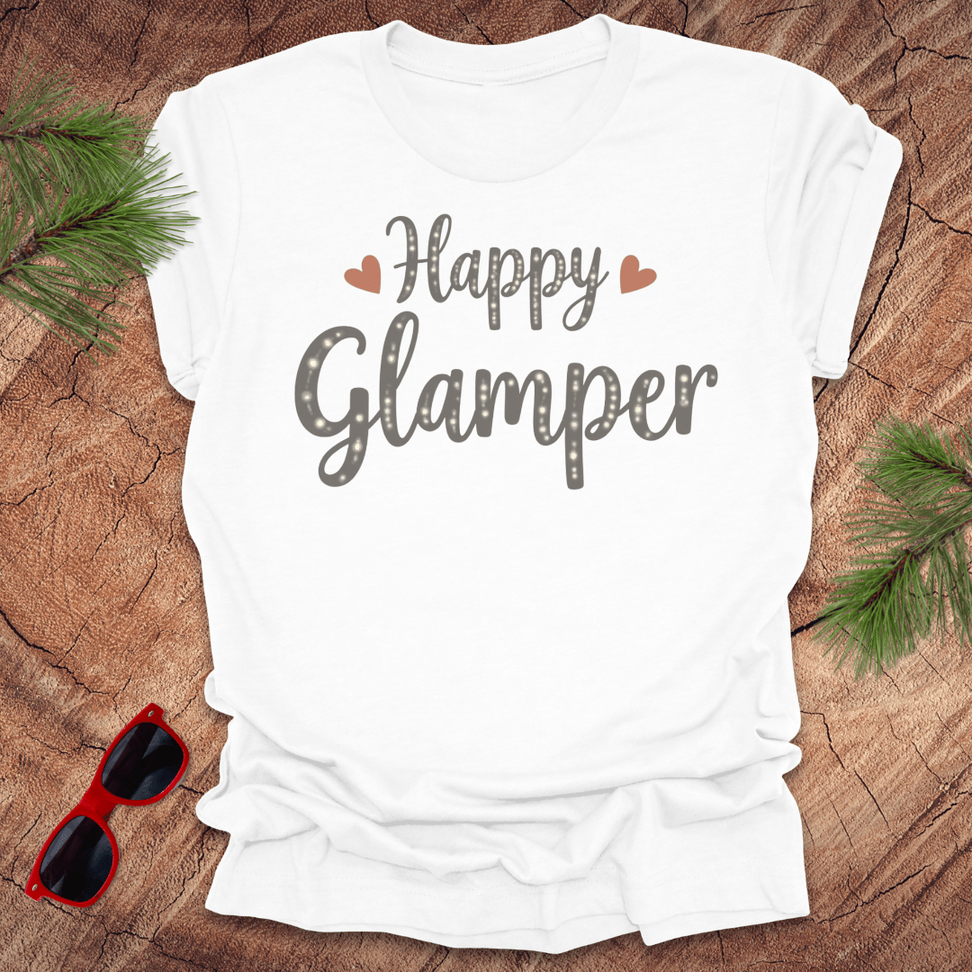 White t-shirt with 'Happy Glamper' text on a wooden surface with sunglasses and pine branches.