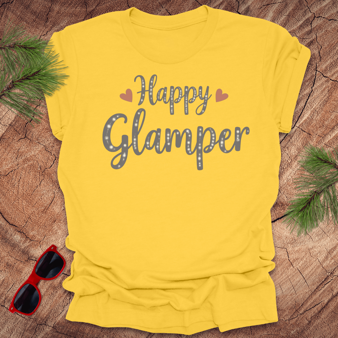 Yellow t-shirt with 'Happy Glamper' text on a wooden surface with sunglasses and greenery.