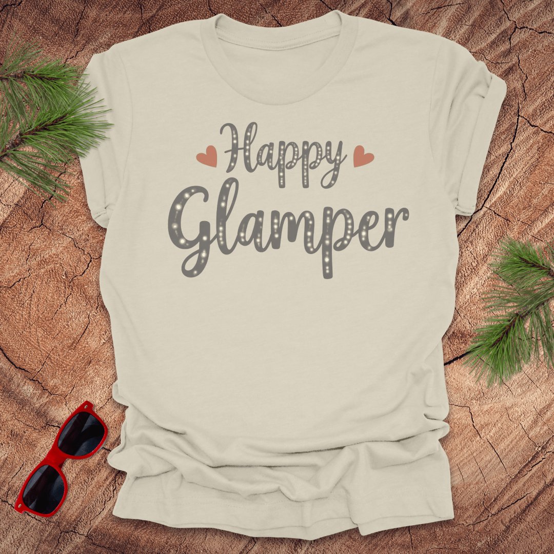 Beige t-shirt with 'Happy Glamper' text on a wooden surface with sunglasses and greenery.