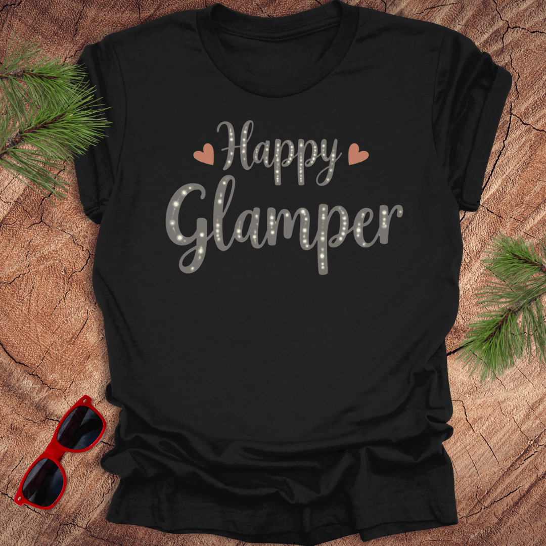 Black t-shirt with 'Happy Glamper' text on a wooden surface with sunglasses and pine branches.