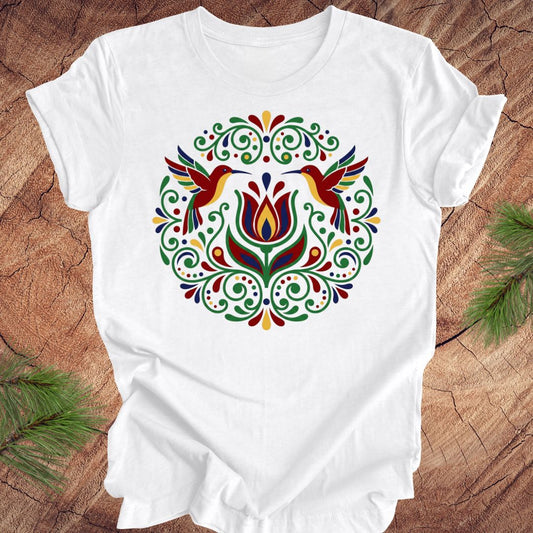 White t-shirt with colorful floral design and hummingbirds on a wooden surface