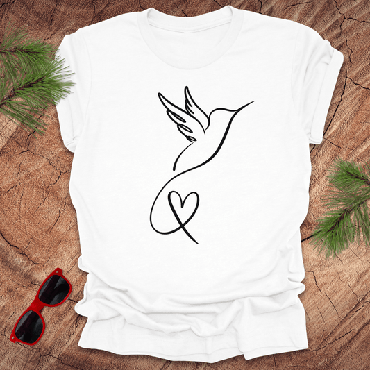 White t-shirt with hummingbird and heart design on a wooden surface with sunglasses and greenery.