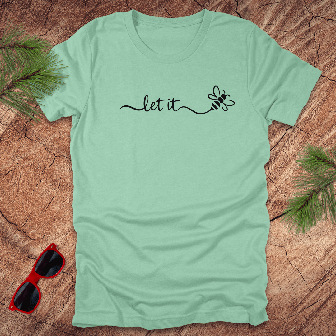 mint green t-shirt with 'let it' text on a wooden surface with sunglasses and greenery.