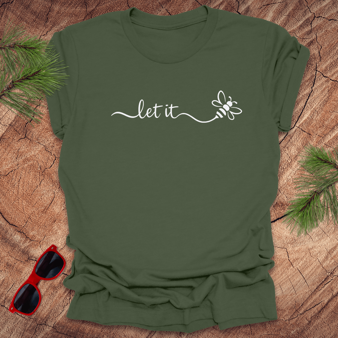 military Green t-shirt with 'let it' text and bee graphic on a wooden surface with sunglasses and pine branches.