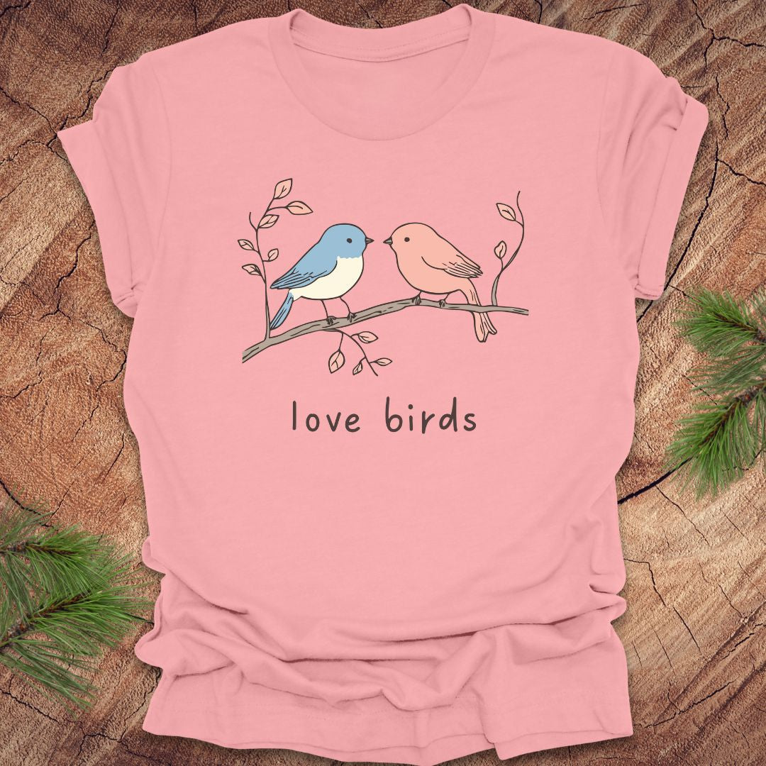Pink t-shirt with a blue and a pink hand drawn bird, on a branch, with text 'love birds' on a wooden background.
