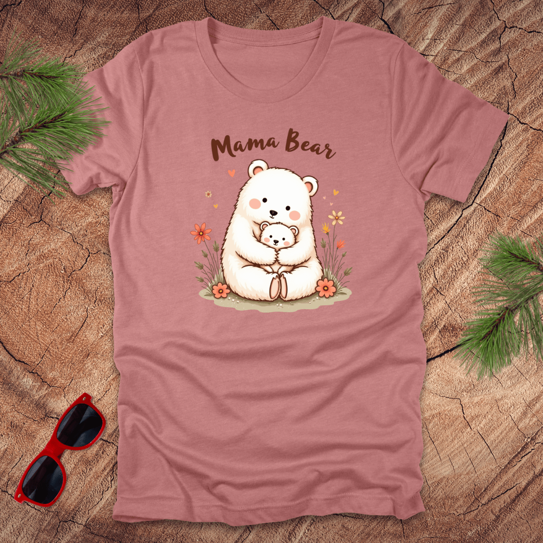 A mauve t-shirt with a graphic of a mama bear holding a cub, accompanied by boho floral details and the text 'Mama Bear'. The shirt is presented on a wood surface with pine needles sunglasses.