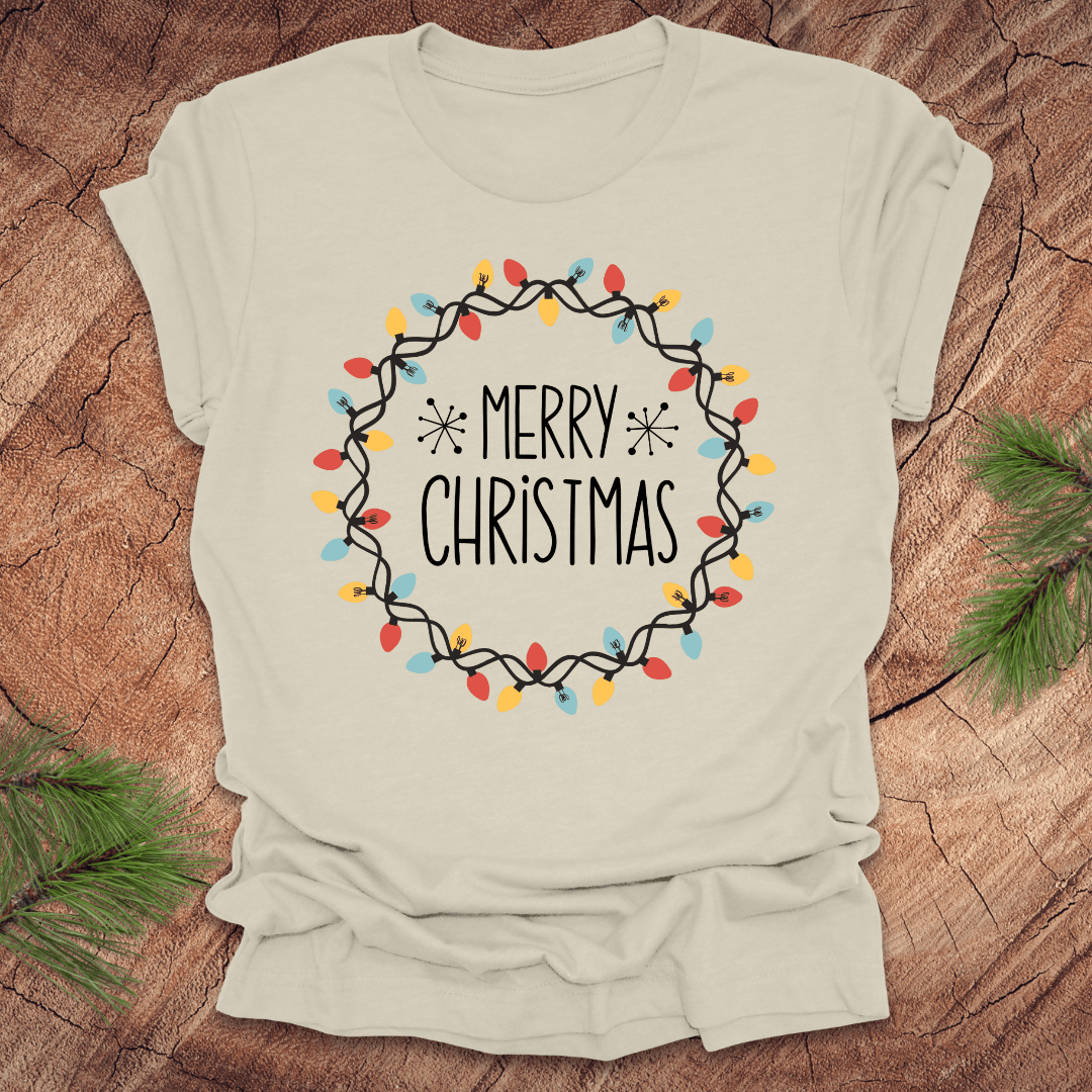 Beige t-shirt with 'Merry Christmas' design on a wooden surface with pine branches.