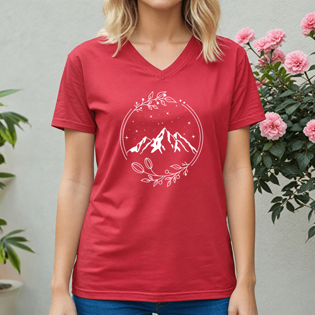 Person wearing a red t-shirt with a mountain design, standing in front of pink flowers and green plants.