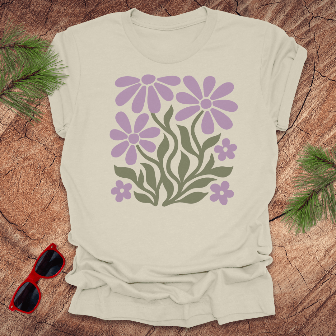 Beige t-shirt with purple floral design on a wooden surface with sunglasses and greenery.