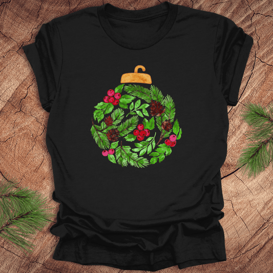 Black t-shirt with a Christmas ornament design featuring green leaves and red berries on a wooden surface.