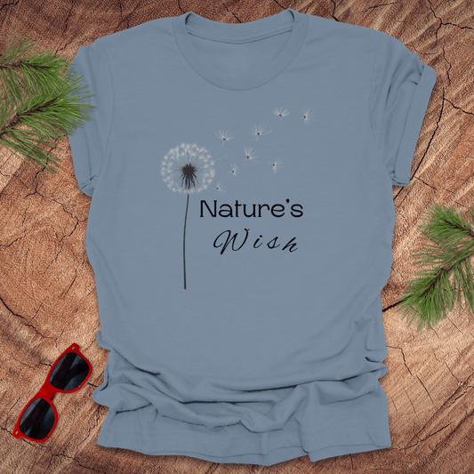 steel blue t-shirt with a dandelion seed design and the text 'Nature's Wish' on the front, presented on a wooden surface with pine needles and red sunglasses.