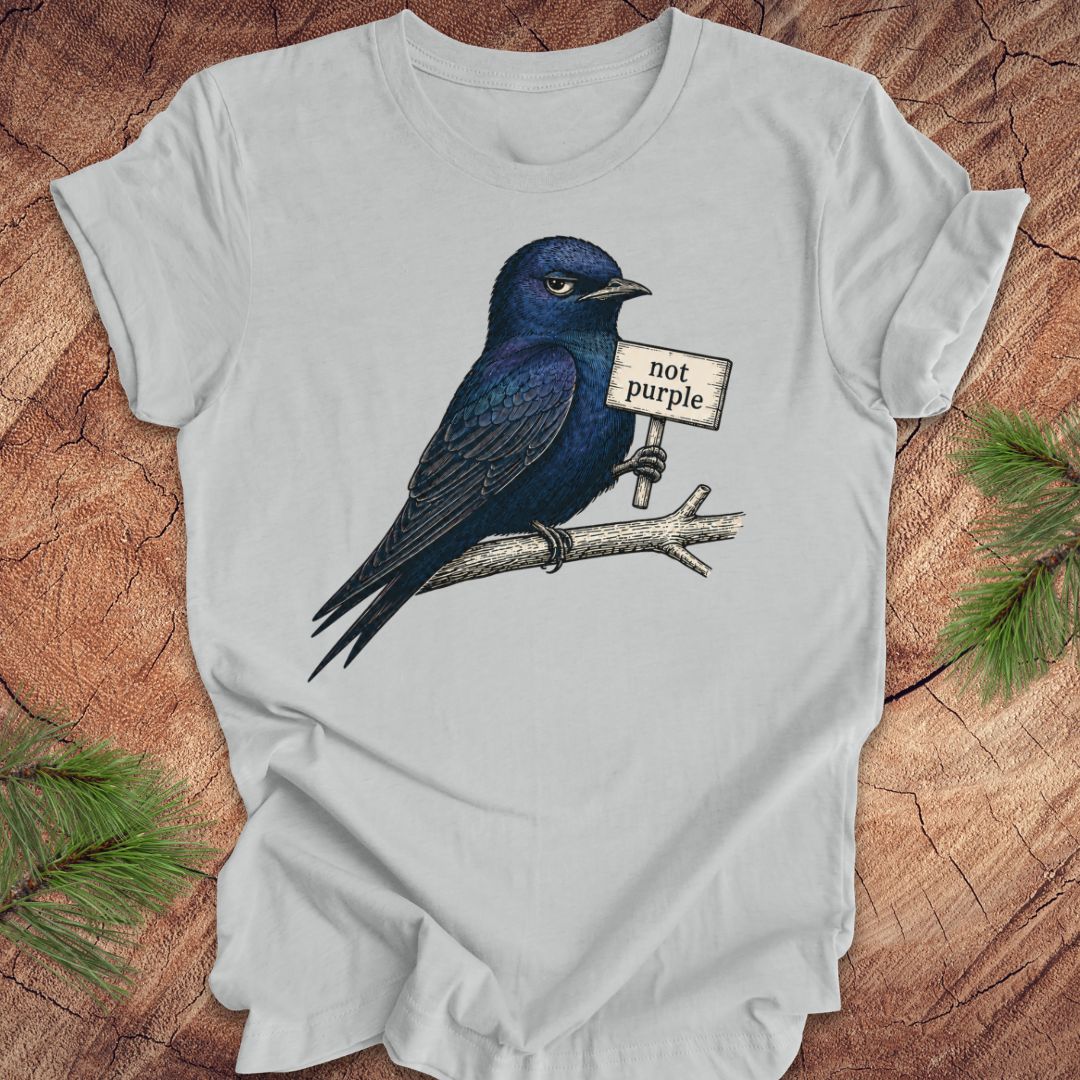 Gray t-shirt with a purple martin bird holding a 'not purple' sign on a wooden surface.
