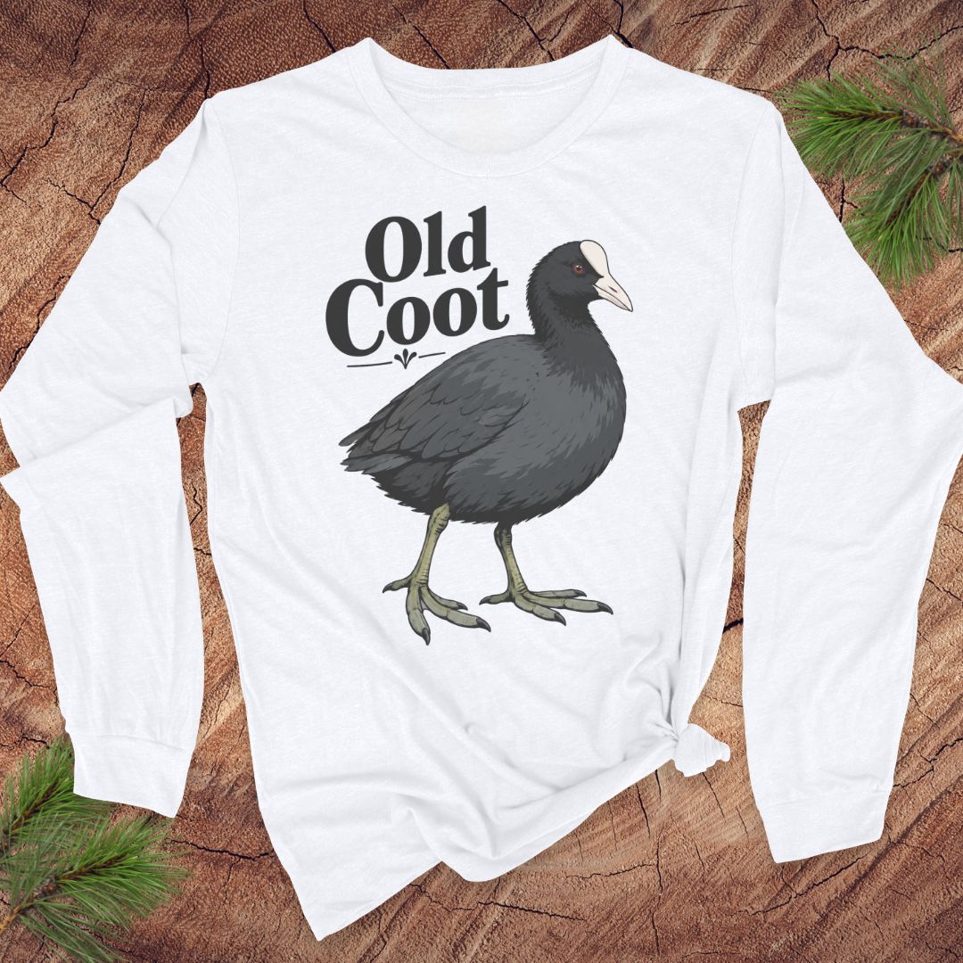 A white long-sleeve t-shirt with a graphic of a dark gray coot and the text 'Old Coot' printed on the front, styled flat on a rustic wood background with pine branches.
