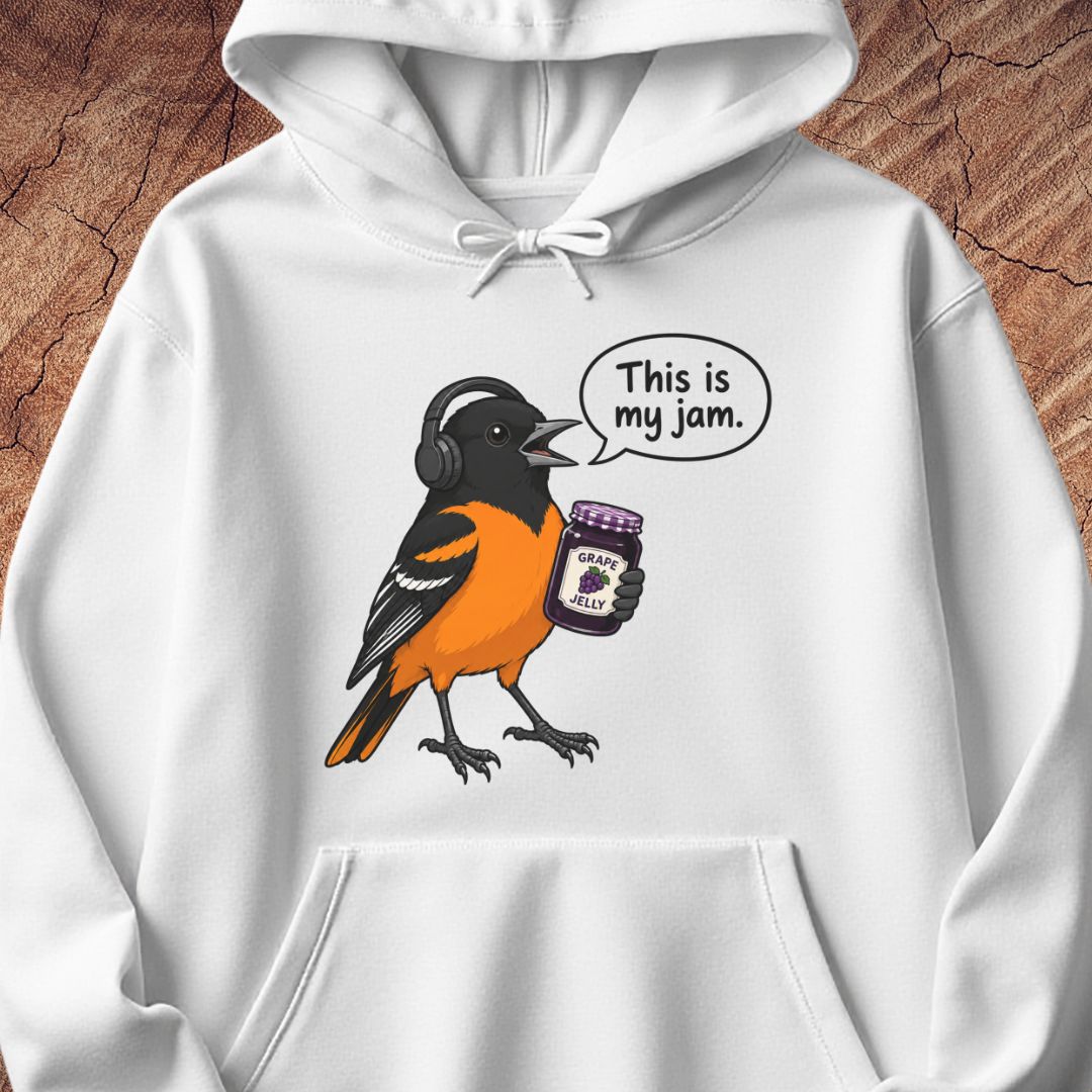 A white pullover hoodie with a graphic of an orange and black bird wearing headphones and holding a jar of jam, with a speech bubble that reads 'This is my jam.' The hoodie is shown against a rustic wood background.