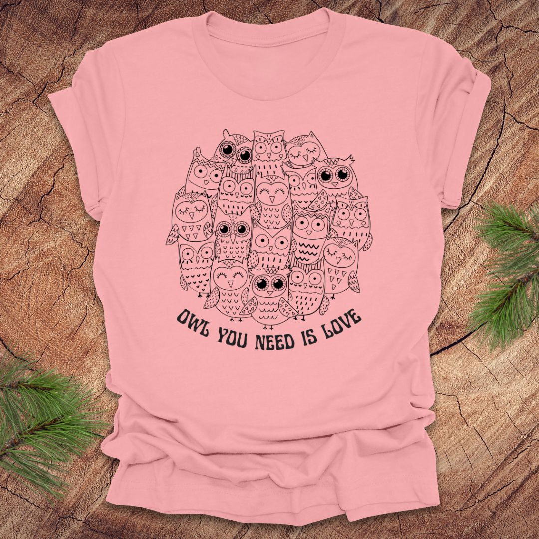 Pink t-shirt with owl design and text 'OWL YOU NEED IS LOVE' on a wooden surface.