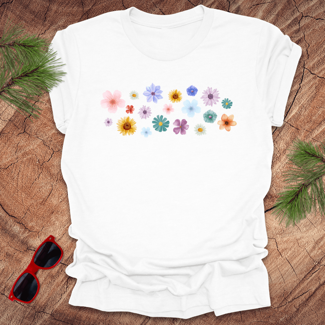 White t-shirt with colorful floral design on a wooden surface with sunglasses and greenery.