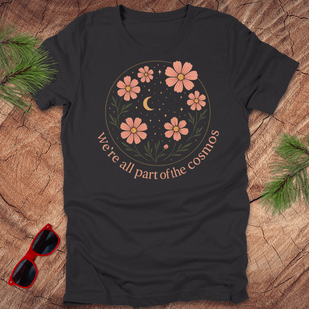 Black t-shirt with floral design and text on a wooden surface with sunglasses and greenery.