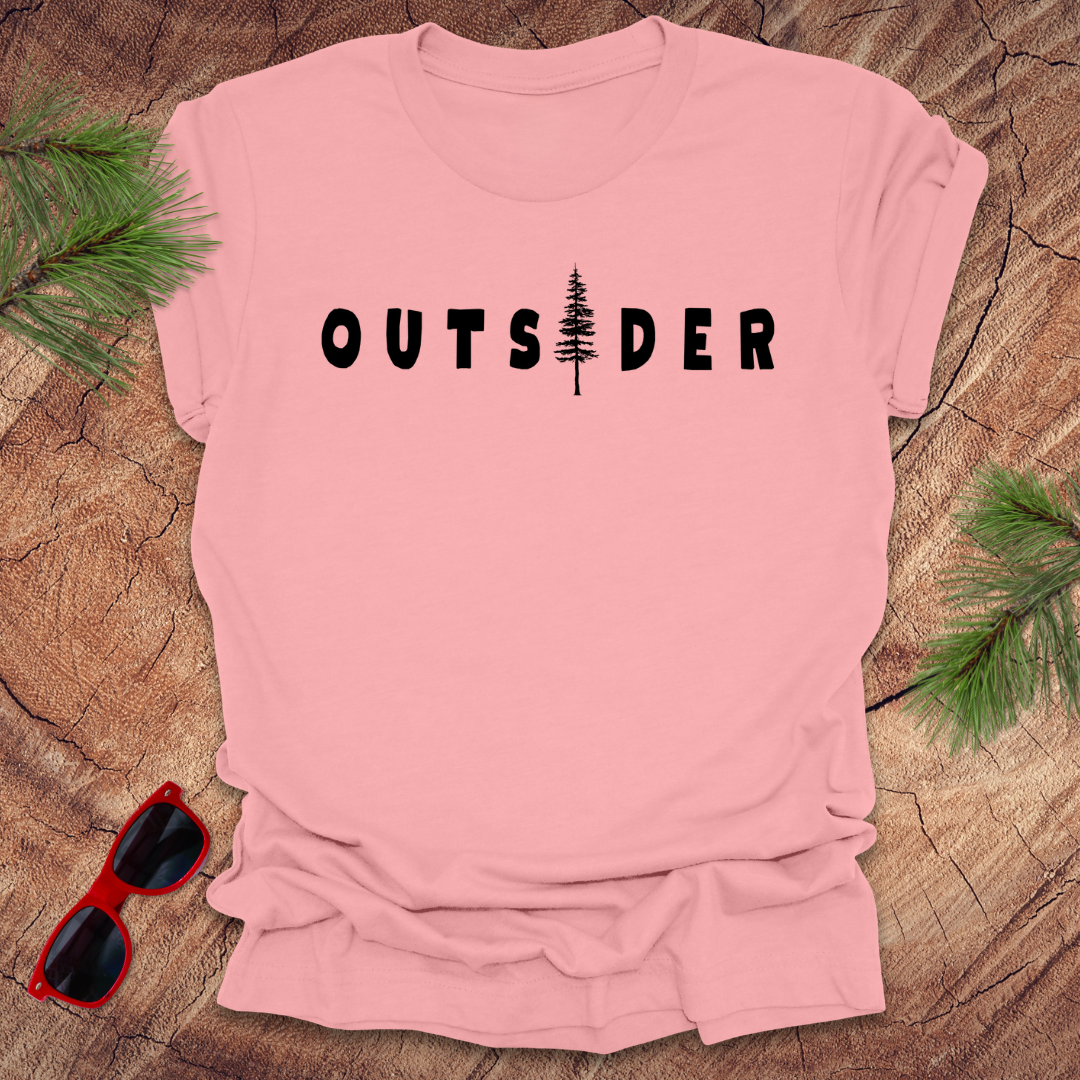 Pink t-shirt with text 'Outsider" the i is a tree, on a wood background with pine branches and sunglasses.