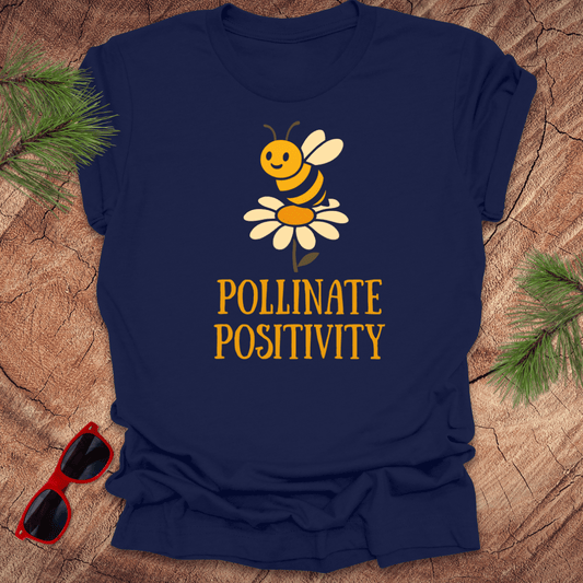 Navy blue t-shirt with a bee and flower graphic and 'Pollinate Positivity' text on a wooden surface.
