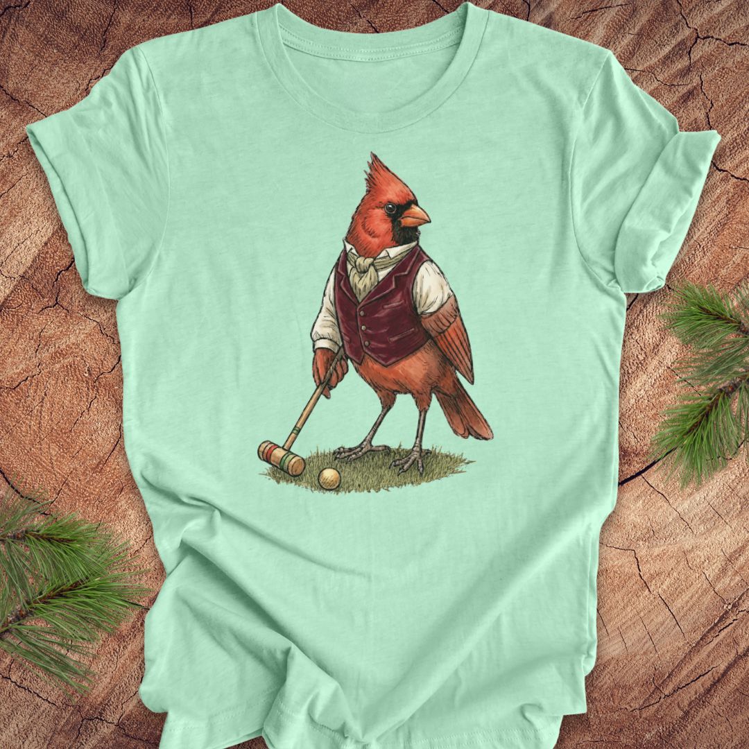 Light green t-shirt with a cardinal playing croquet design on a wooden surface.