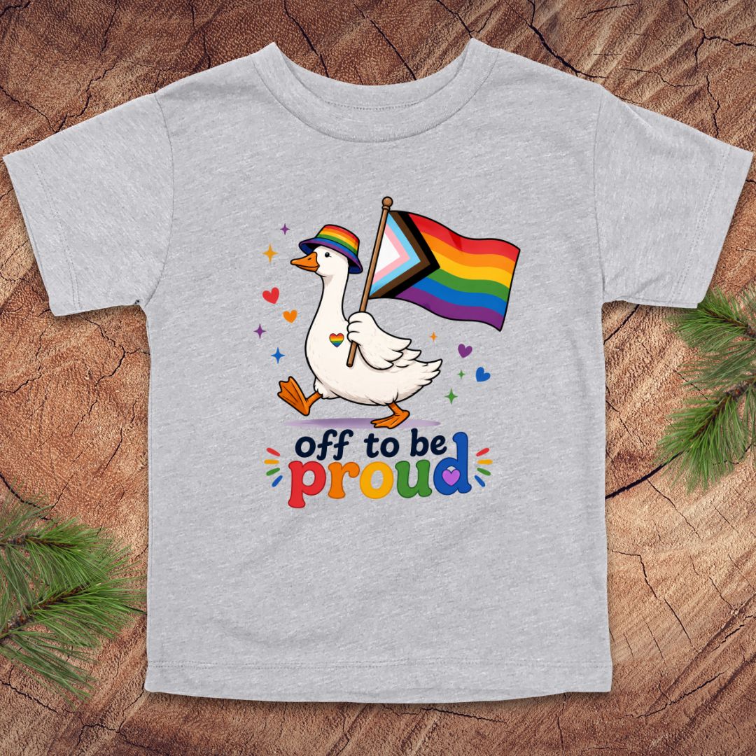 Gray t-shirt with a colorful graphic of a duck holding a rainbow flag and text 'off to be proud' on a wooden surface.