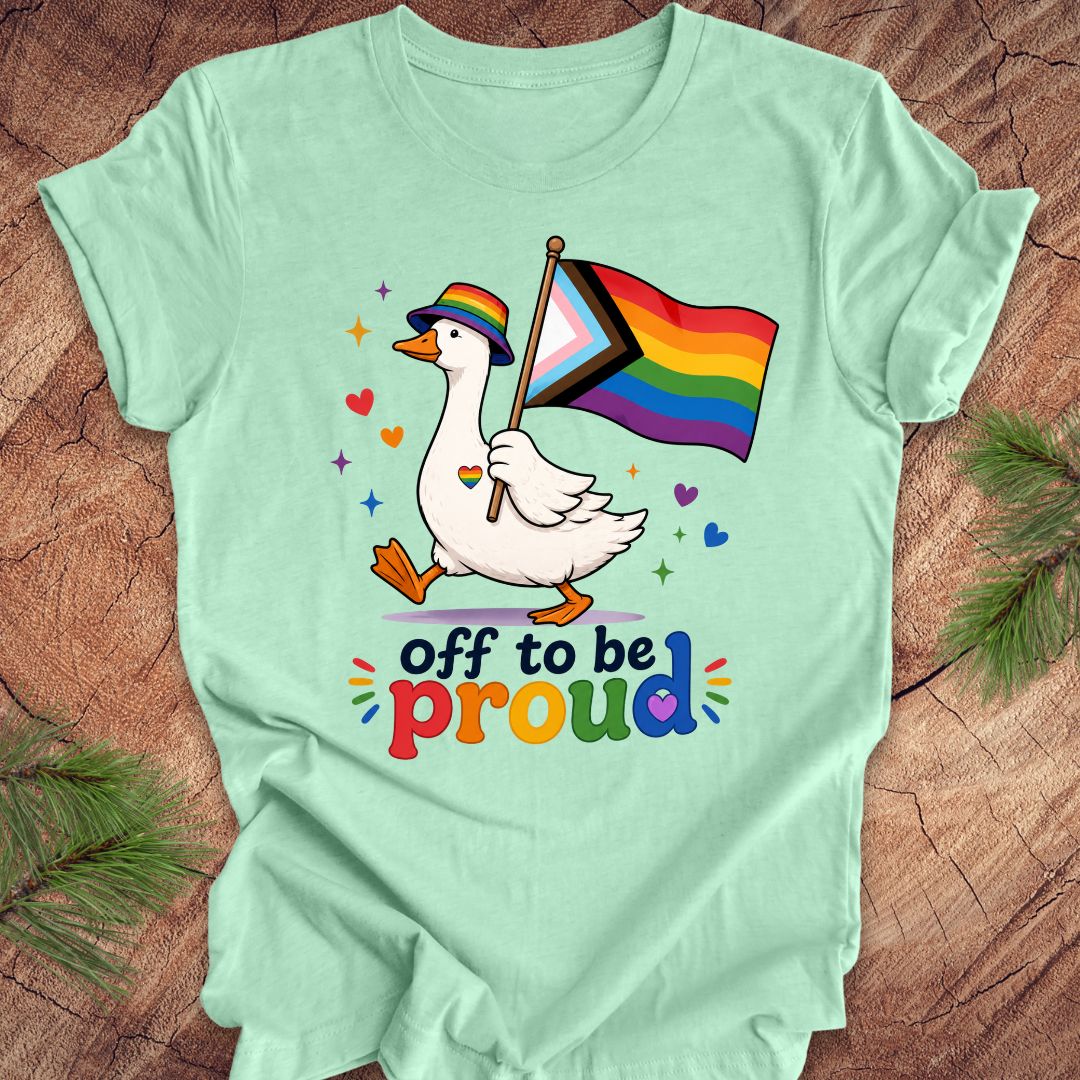 Mint green t-shirt with a goose holding a rainbow flag and 'off to be proud' text on a wooden surface.
